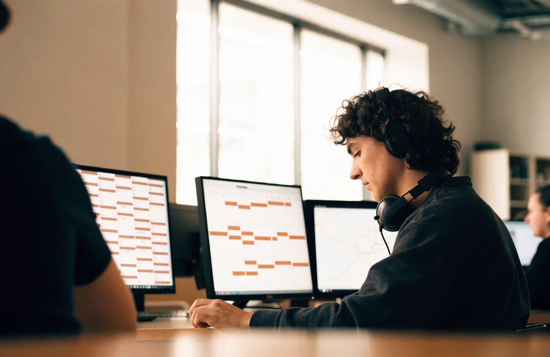A dispatcher managing a scheduling board and map across three monitors