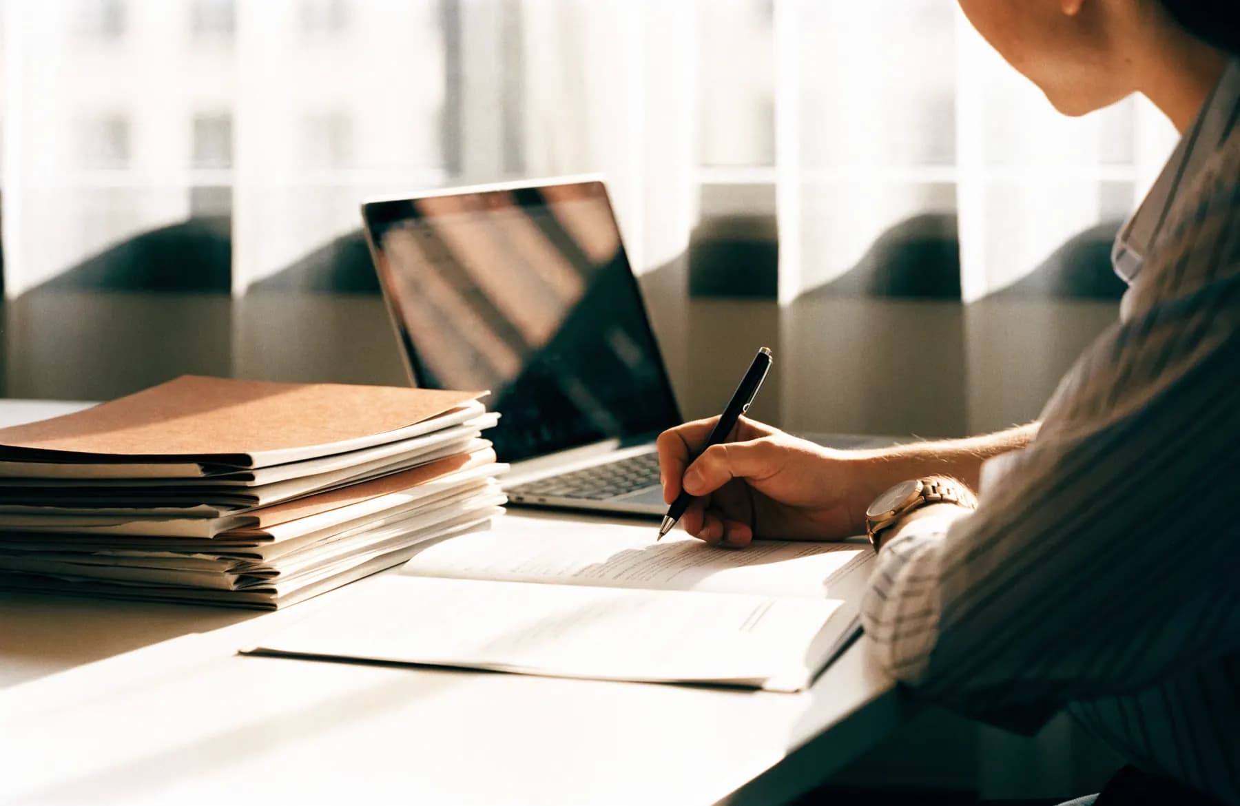 A reviewer working through a stack of document folders beside a laptop