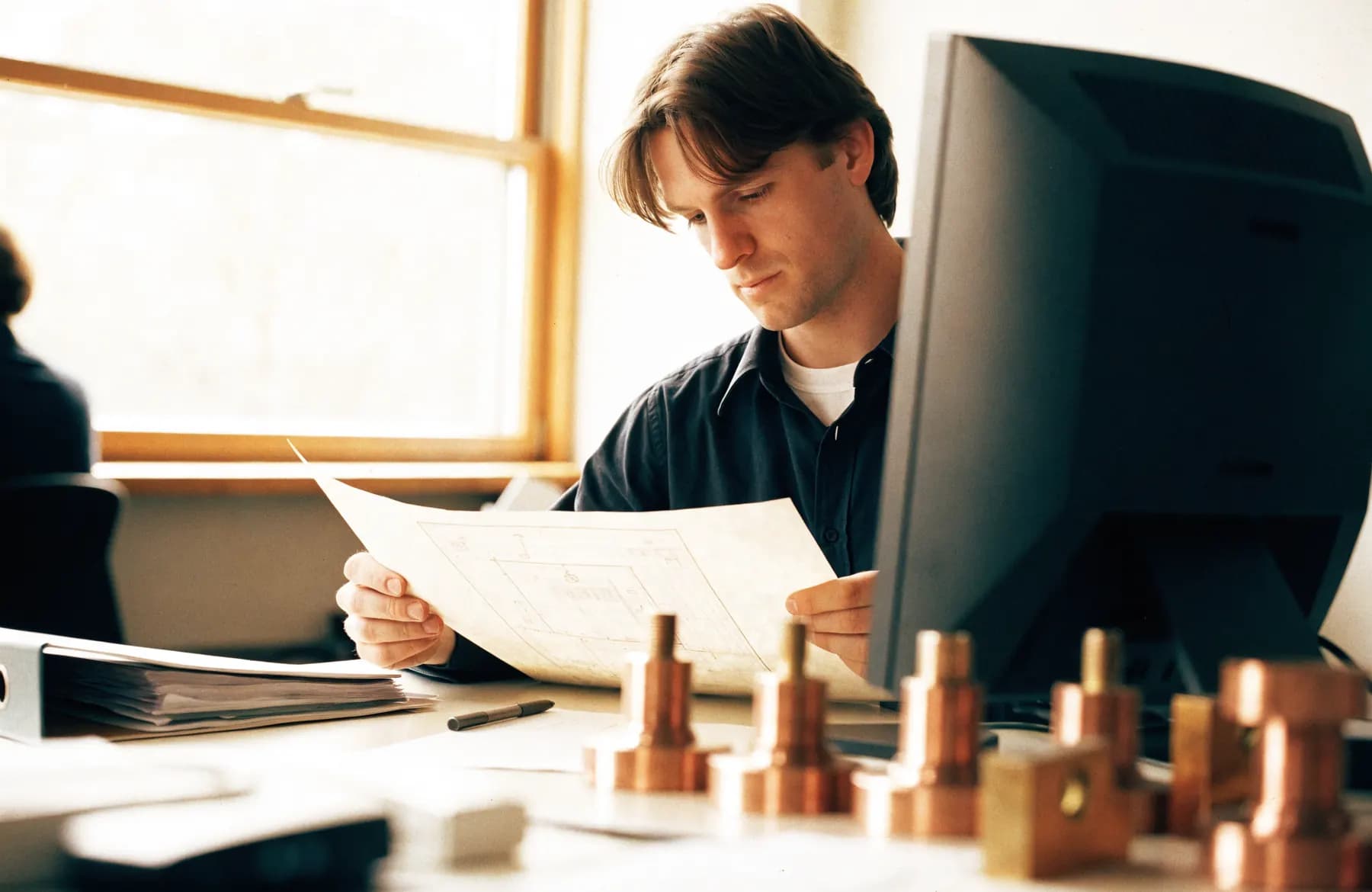 A sales engineer reviewing a technical drawing beside a monitor in an industrial supplier's office