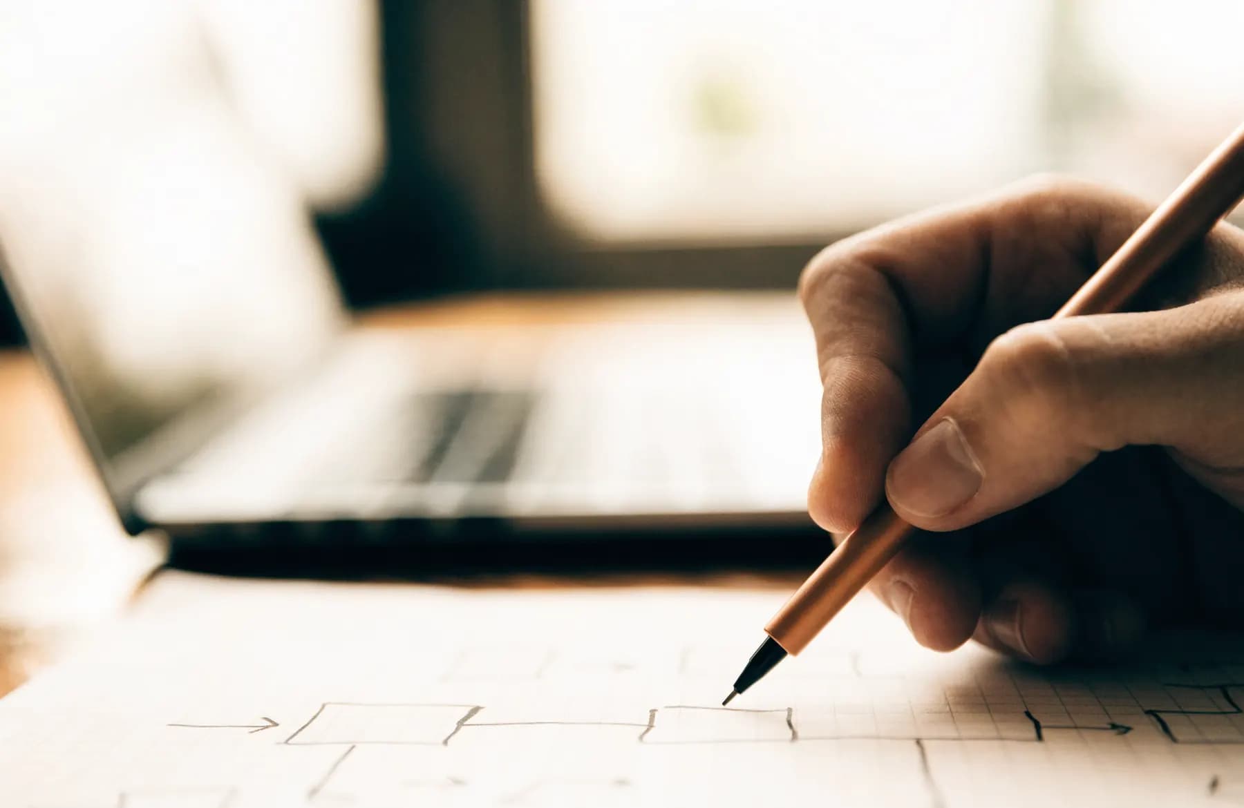 A hand sketching a system architecture diagram of boxes and arrows on grid paper