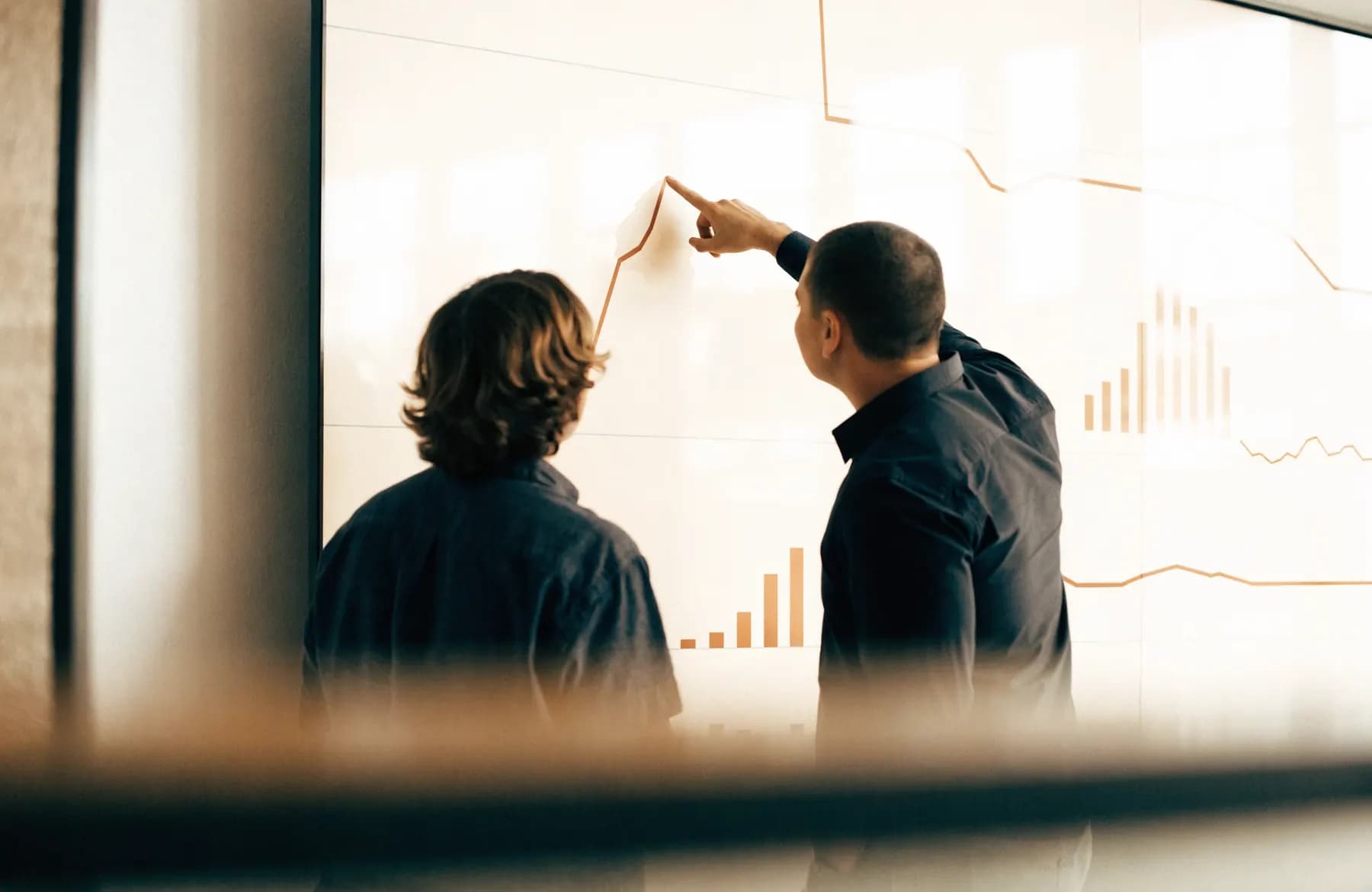 Two engineers reviewing infrastructure monitoring graphs on a wall display