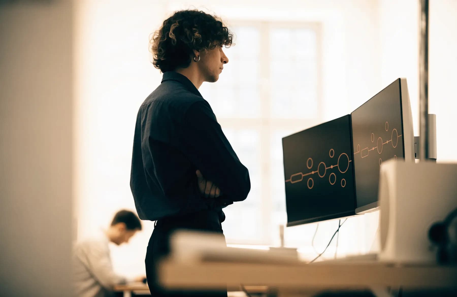 An engineer reviewing data pipeline flow diagrams on two large monitors