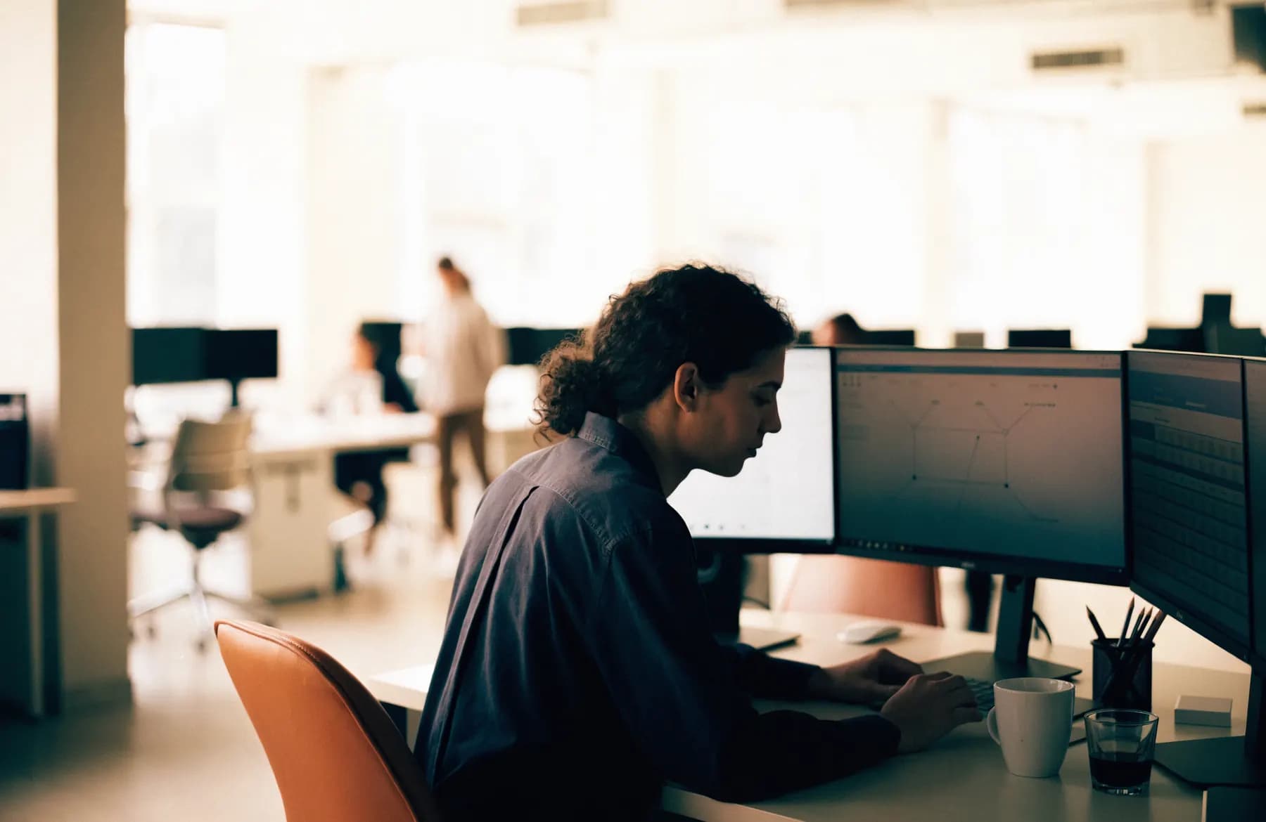 An operations analyst working across three monitors showing workflow status boards