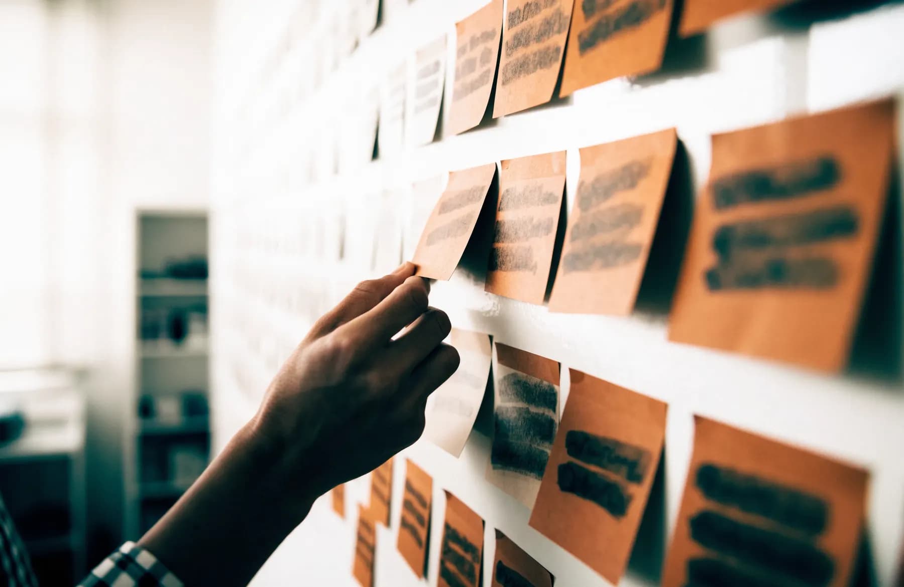 A hand moving an index card on a project planning wall arranged in columns